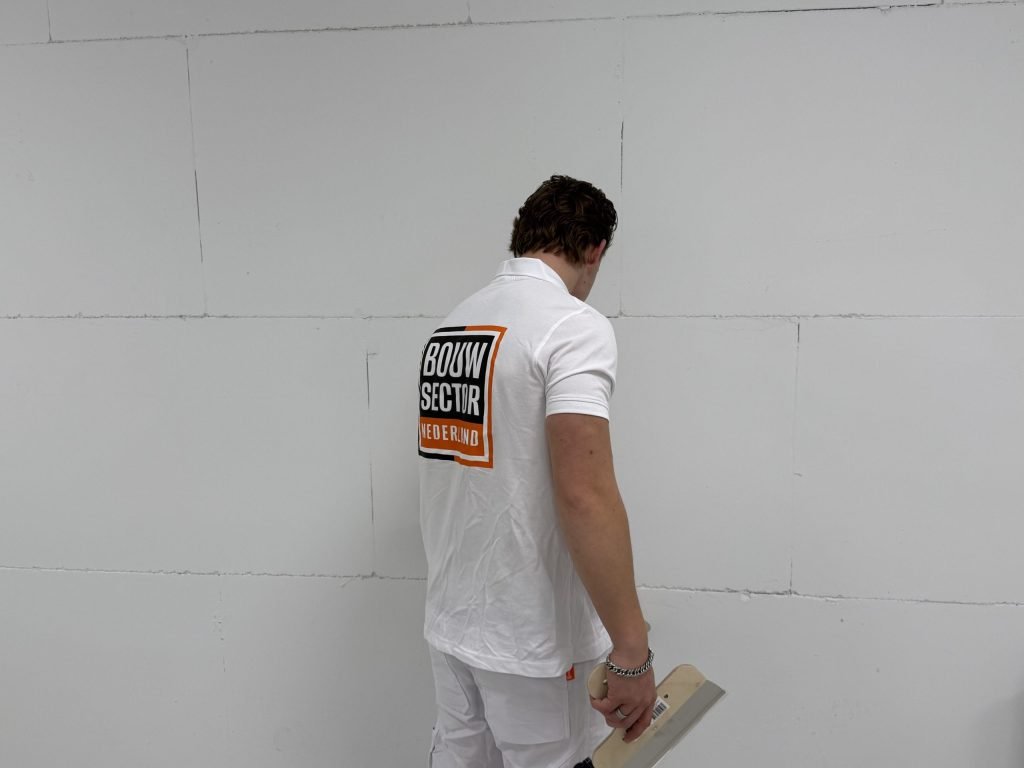 Stukadoor met een plamuurmes in zijn hand bekijkt van dichtbij de naden van een witte wand