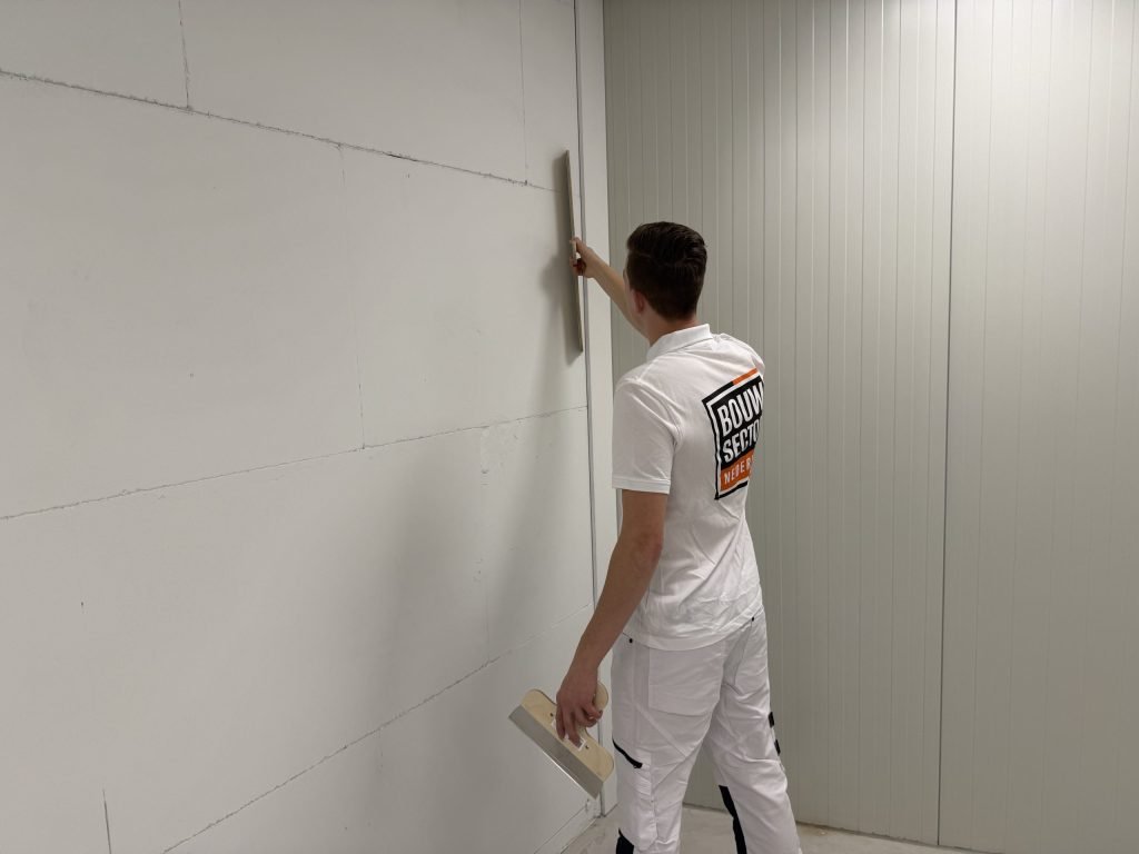 Stukadoor loopt met een rei langs een wand van gipsblokken en controleert of de wand vlak is