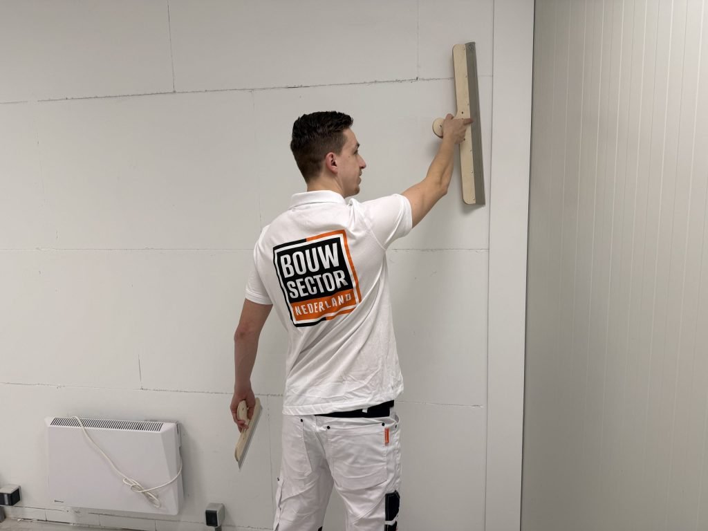 Stukadoor kijkt opzij naar de spaan die hij hoog tegen een witte wand drukt