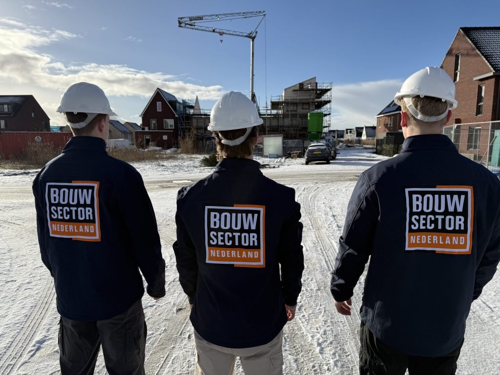 Drie vakmensen van Bouwsector Nederland met witte helm op een nieuwbouwterrein met woningen in aanbouw